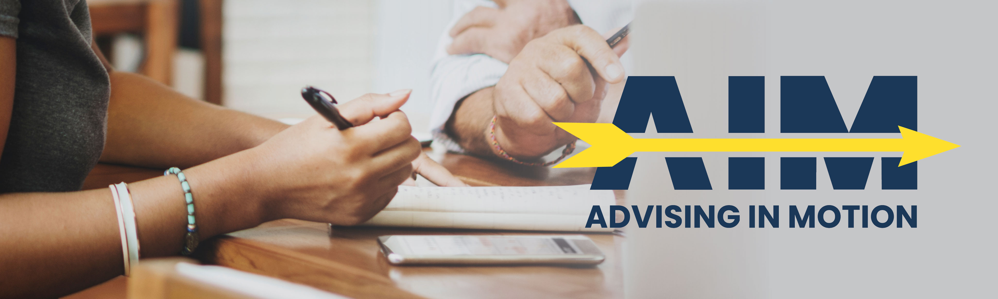 An image of two sets of hands with pens working on a project with the Advising in Motion QEP Logo on the right side.