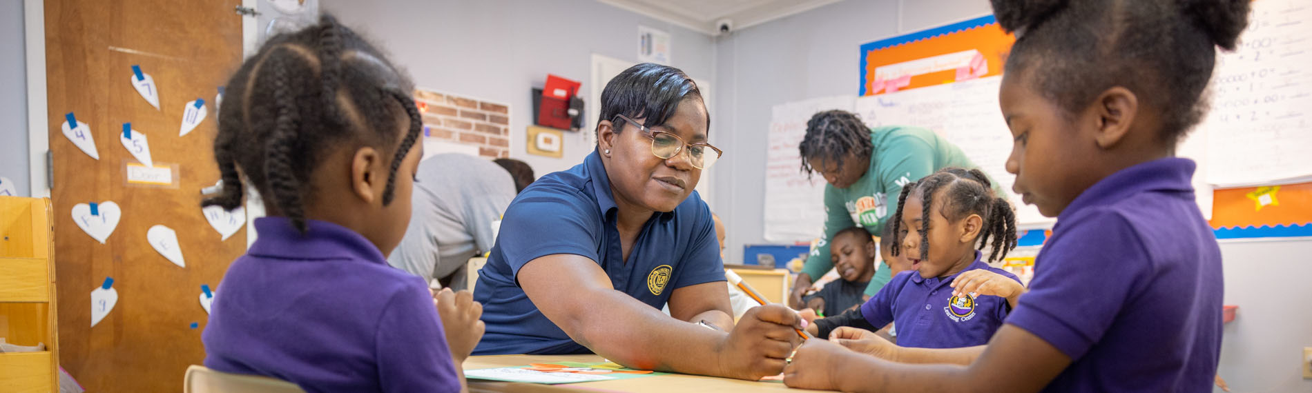 A FDTC Early Childhood Graduate help a child in a classroom.