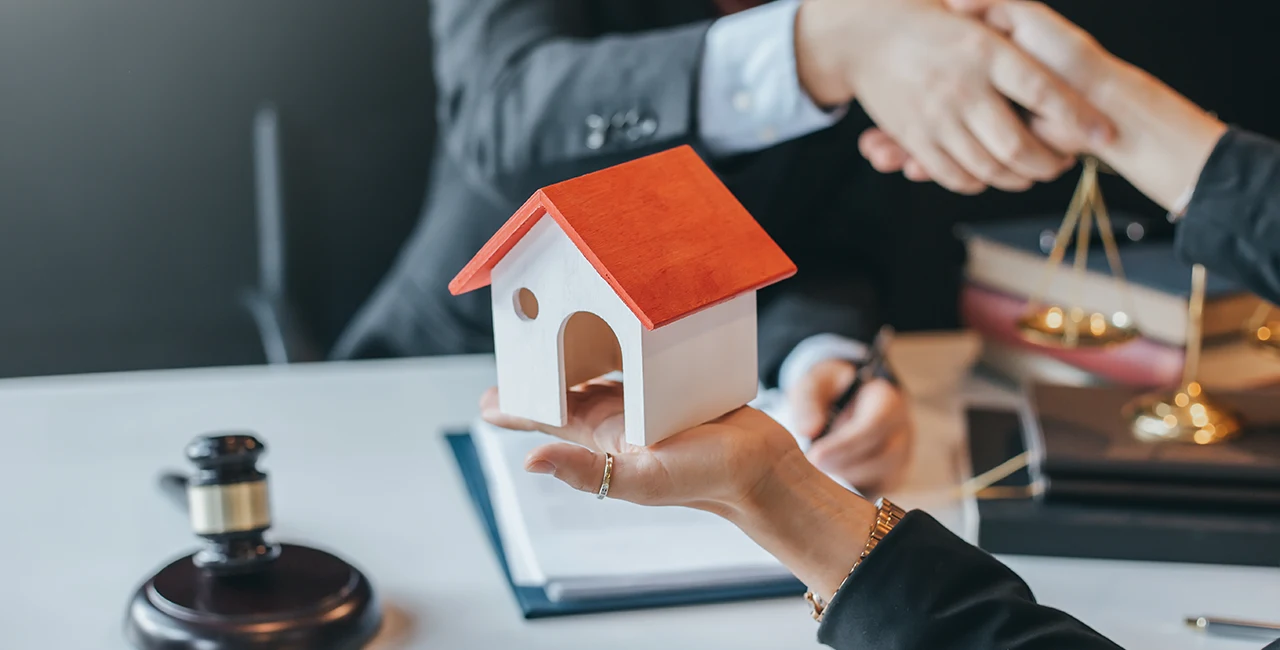 A real estate agent and a home buyer seal the deal while the home buyer holds a model house.